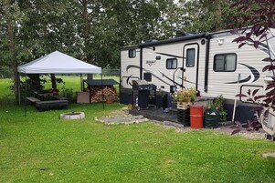 A recreational vehicle with a covered outdoor area, a grill, and a fire pit.