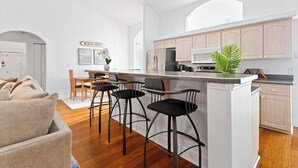 Een moderne keuken met een centraal eiland, barkrukken en een bord waarop 'BEACH HOUSE' staat.