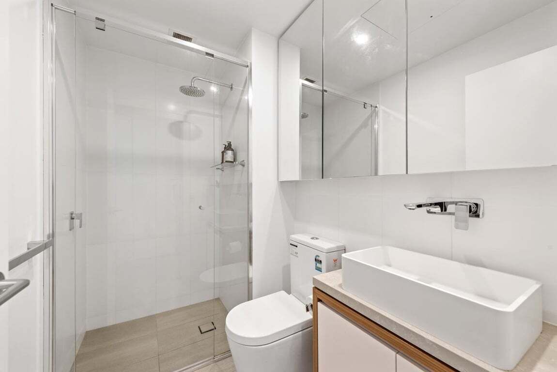 A modern bathroom with a glass shower enclosure, a white toilet, and a large rectangular sink.