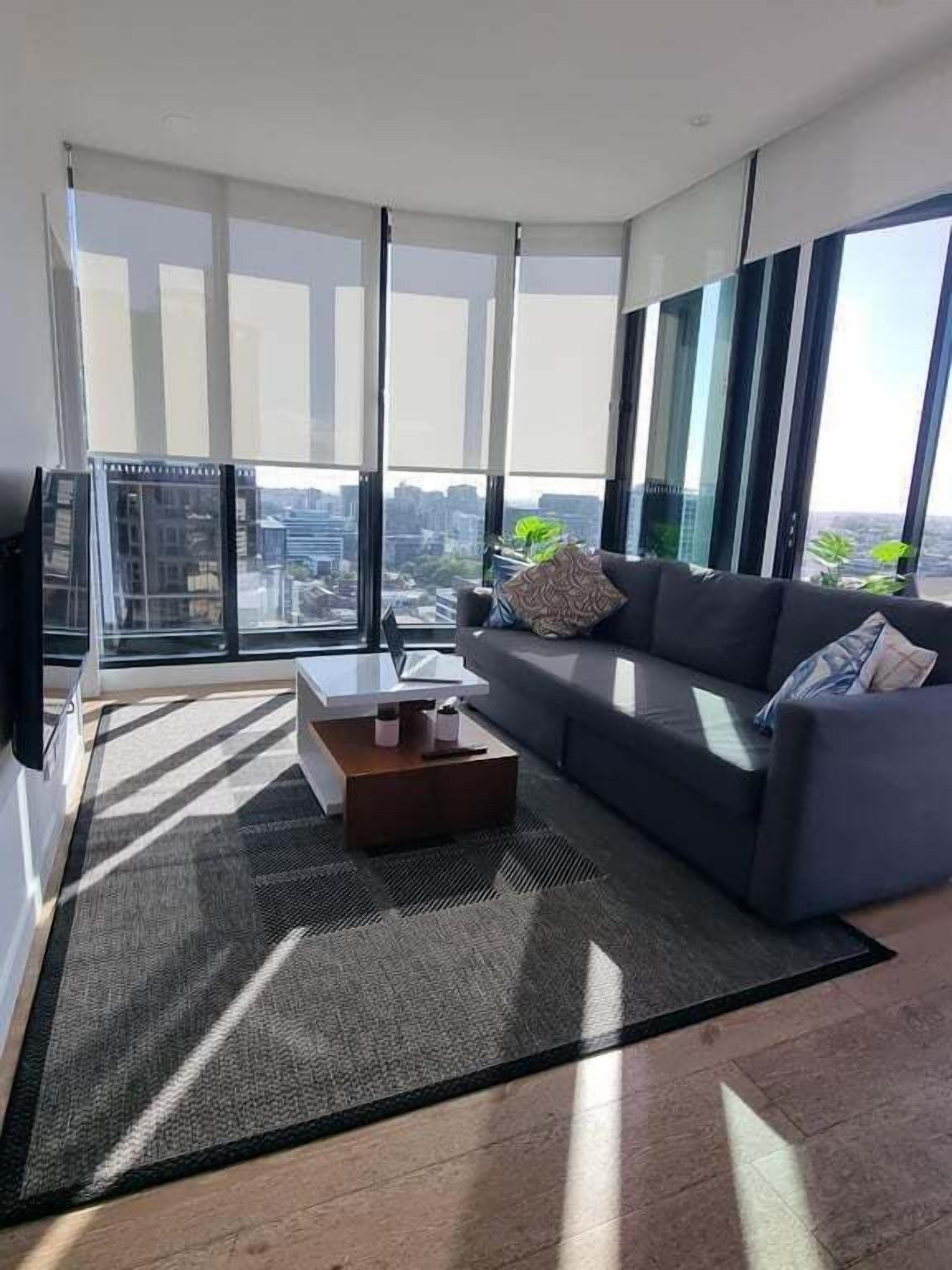 A modern living room with a sofa, coffee table, and large windows offering a city view.