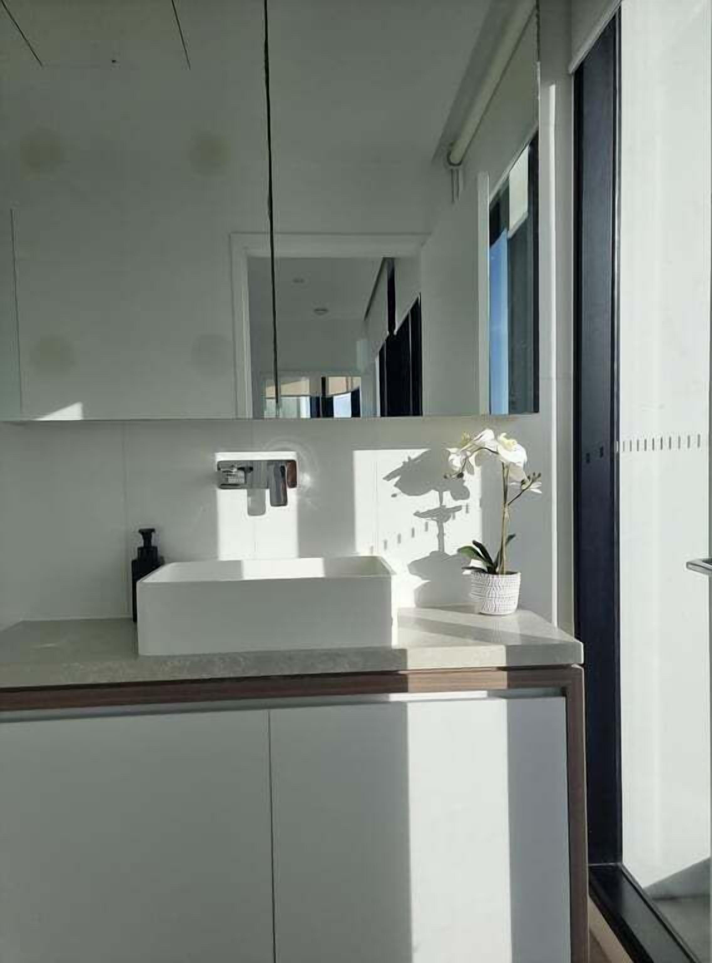 Une salle de bain moderne avec un grand miroir, un lavabo blanc et une orchidée en pot.