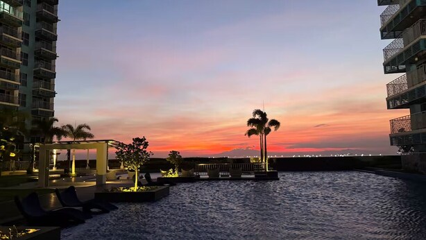 A waterfront hotel with a sunset view, outdoor seating, and palm trees. - Deluxe Apartment Balcony Sea View (Parañaque)
