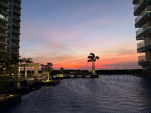 Un hotel frente al agua con vista al atardecer, asientos al aire libre y palmeras.