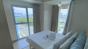 A hotel room with a large bed, a view of a parking lot and buildings, and a window with curtains. - Deluxe Apartment Balcony Sea View (Parañaque)