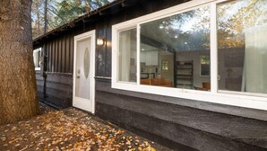 Een chalet met een groot raam, een deur en een boom op de voorgrond.
