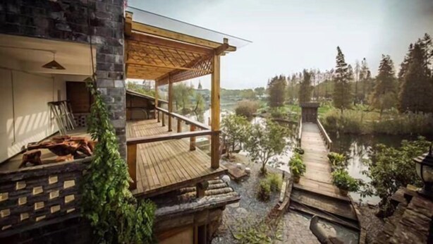 A modern building with a wooden deck overlooking a body of water, surrounded by greenery. - Yayunju Inn (Shanghai)