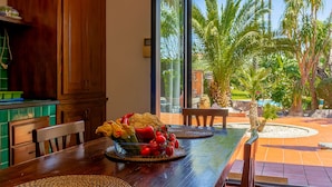 A dining area with a wooden table, chairs, and a view of palm trees through a glass door. - Villa Gialla Private Padel Court (Aci Sant'Antonio)
