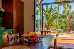 Un coin repas avec une table en bois, des chaises et une vue sur les palmiers, visible à travers une porte vitrée.