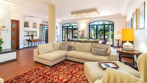 A spacious living area with a large beige sectional sofa, a red patterned rug, and a dining area with a table and chairs. - Villa Gialla Private Padel Court (Aci Sant'Antonio)