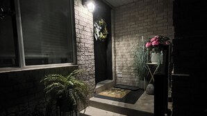 Ein gut beleuchteter Eingangsbereich mit Backsteinwand, Fenster, einer Tür mit Girlande und einer kleinen Stufe zum Eingang.