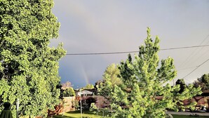 Ein Wohngrundstück mit Rasen, Bäumen, einem Haus und einem sichtbaren Regenbogen.