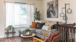 Ein Wohnzimmer mit grauem Sofa, Couchtisch, Pflanze, Gemälde und einer Treppe.