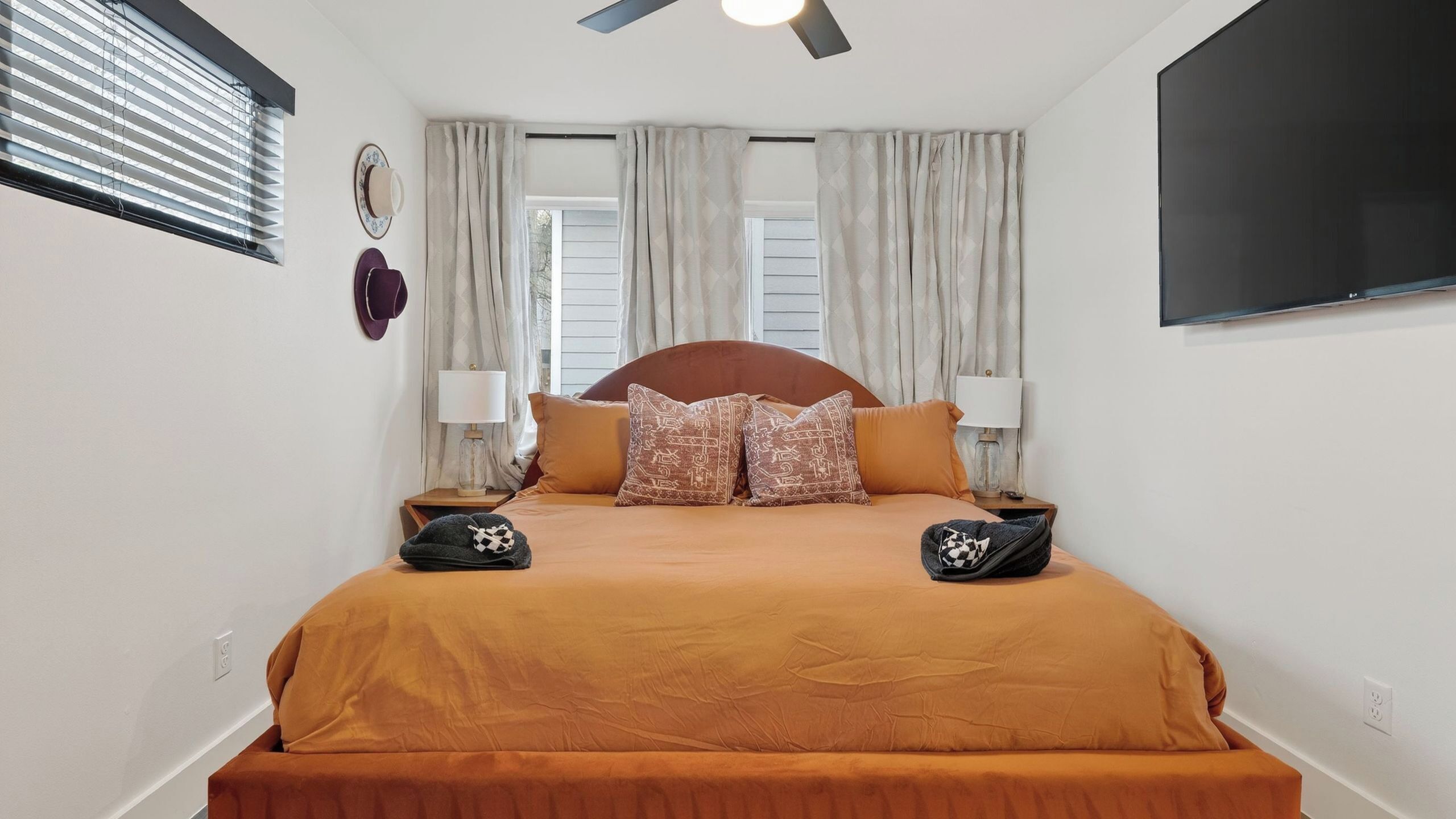 A bedroom with a bed, two bedside tables, a ceiling fan, and a TV mounted on the wall.
