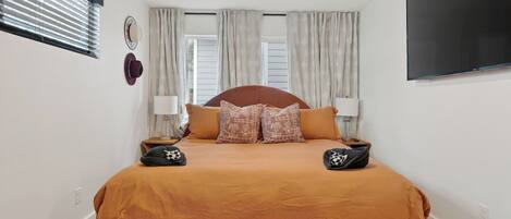 A bedroom with a bed, two bedside tables, a ceiling fan, and a TV mounted on the wall.
