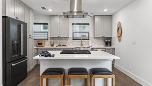 A modern kitchen with a large island, bar stools, a built-in oven, and a stainless steel refrigerator. - Eastside Keys by Avantstay Bright East Austin Stay + Backyard Dining + Near 6th St and Downtown (Austin)