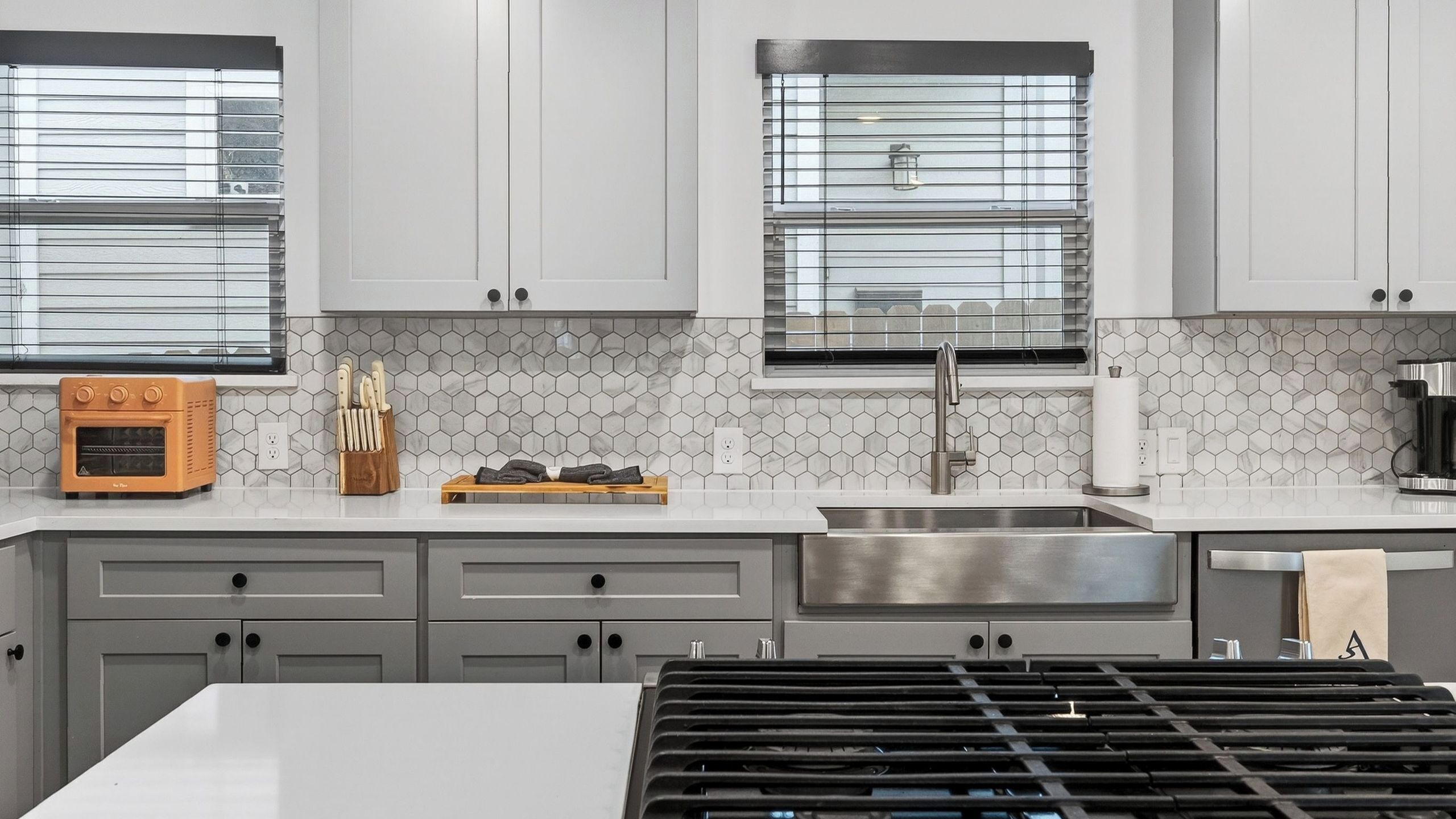 A modern kitchen with grey cabinets, a built-in oven, a stainless steel sink, and a gas range.