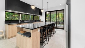 Cozinha moderna com uma ilha grande, banquetas pretas e vista para o verde através da porta de vidro.