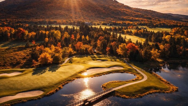 Um campo de golfe com uma ponte sobre um lago, cercado por folhagem outonal e uma montanha ao fundo.