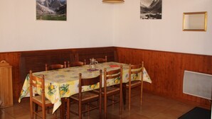 Een eethoek met een tafel gedekt voor zes personen, houten stoelen, een houten bank en twee ingekaderde afbeeldingen aan de muur.