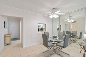 A dining area with a glass table, metal chairs, a ceiling fan, and a large mirror reflecting the room. - Beach Getaway in Pompano! 2BR/2BA Condo – Walk to Beach & Restaurants, groceries (Pompano Beach)