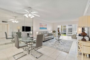 A modern living room with a glass dining table, leather sofa, and a ceiling fan. - Beach Getaway in Pompano! 2BR/2BA Condo – Walk to Beach & Restaurants, groceries (Pompano Beach)