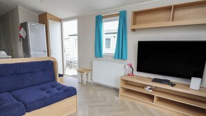 Una sala de estar con sofá, televisor, estanterías de madera y una ventana con cortinas.