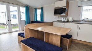 Una kitchenette compacta con microondas, tostadora y hervidor, un banco con asiento acolchado y un ventanal corredero que da al exterior.