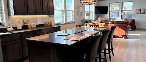 Una cocina moderna con armarios oscuros, una isla central con taburetes y lámparas colgantes.