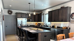 Una cocina moderna con armarios oscuros, electrodomésticos de acero inoxidable, una isla central con taburetes y luminarias colgantes.