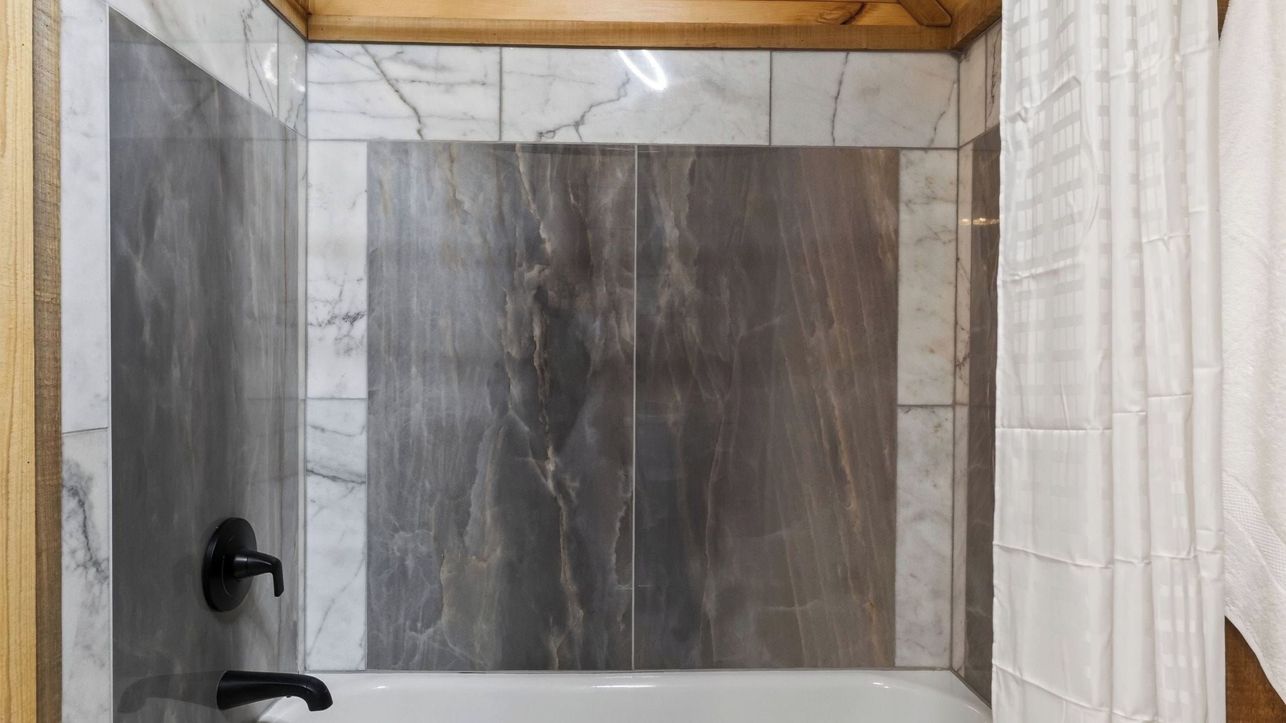 Ein Badezimmer mit Badewanne, Marmorwänden und Holzbalken an der Decke.