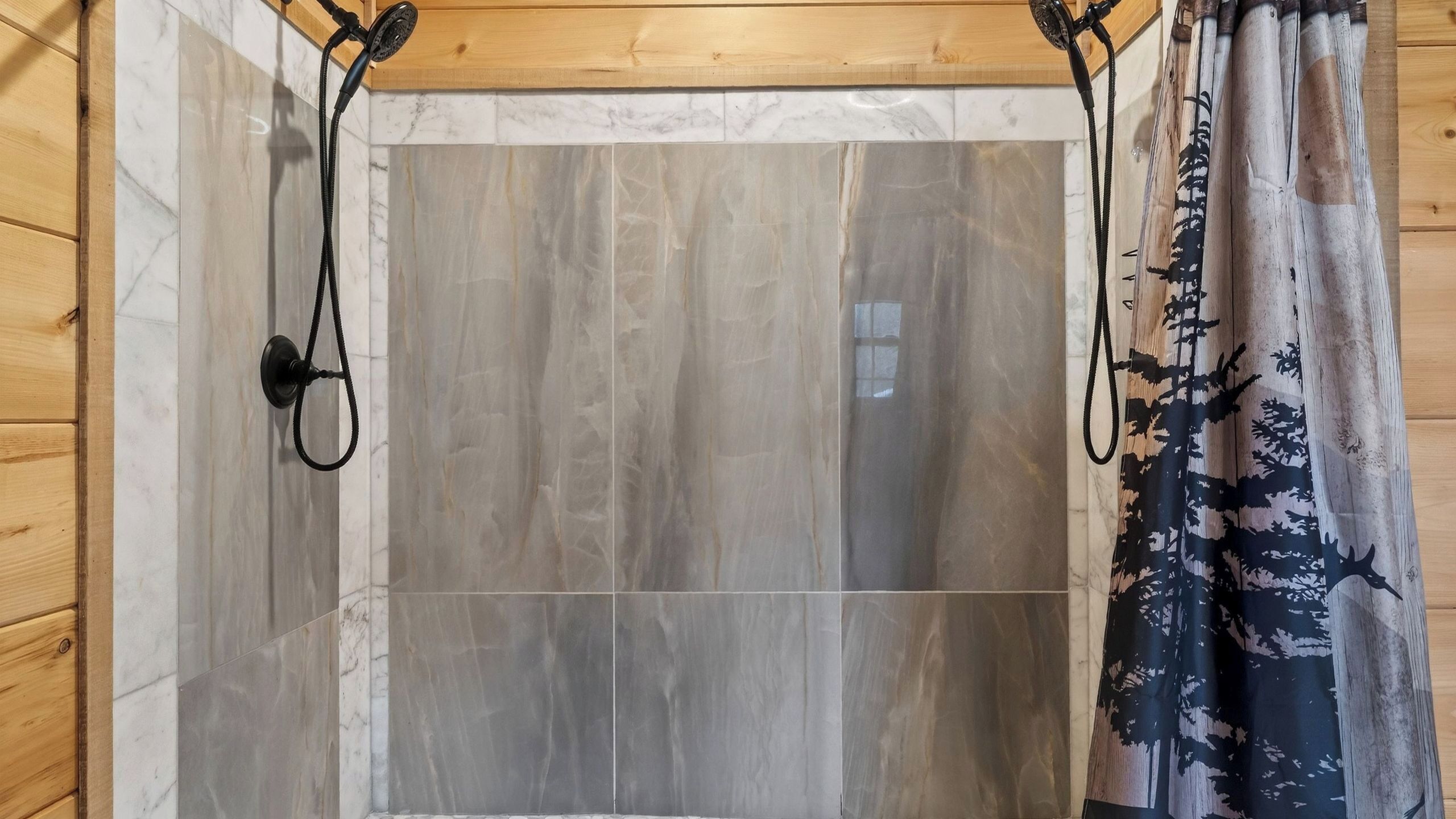 A shower area with a wooden ceiling, a shower curtain with a forest pattern, and a towel rack.