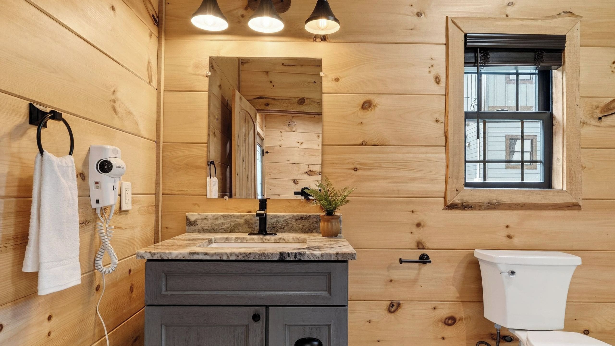A wooden cabin bathroom with a marble sink, a toilet, and a window with blinds.
