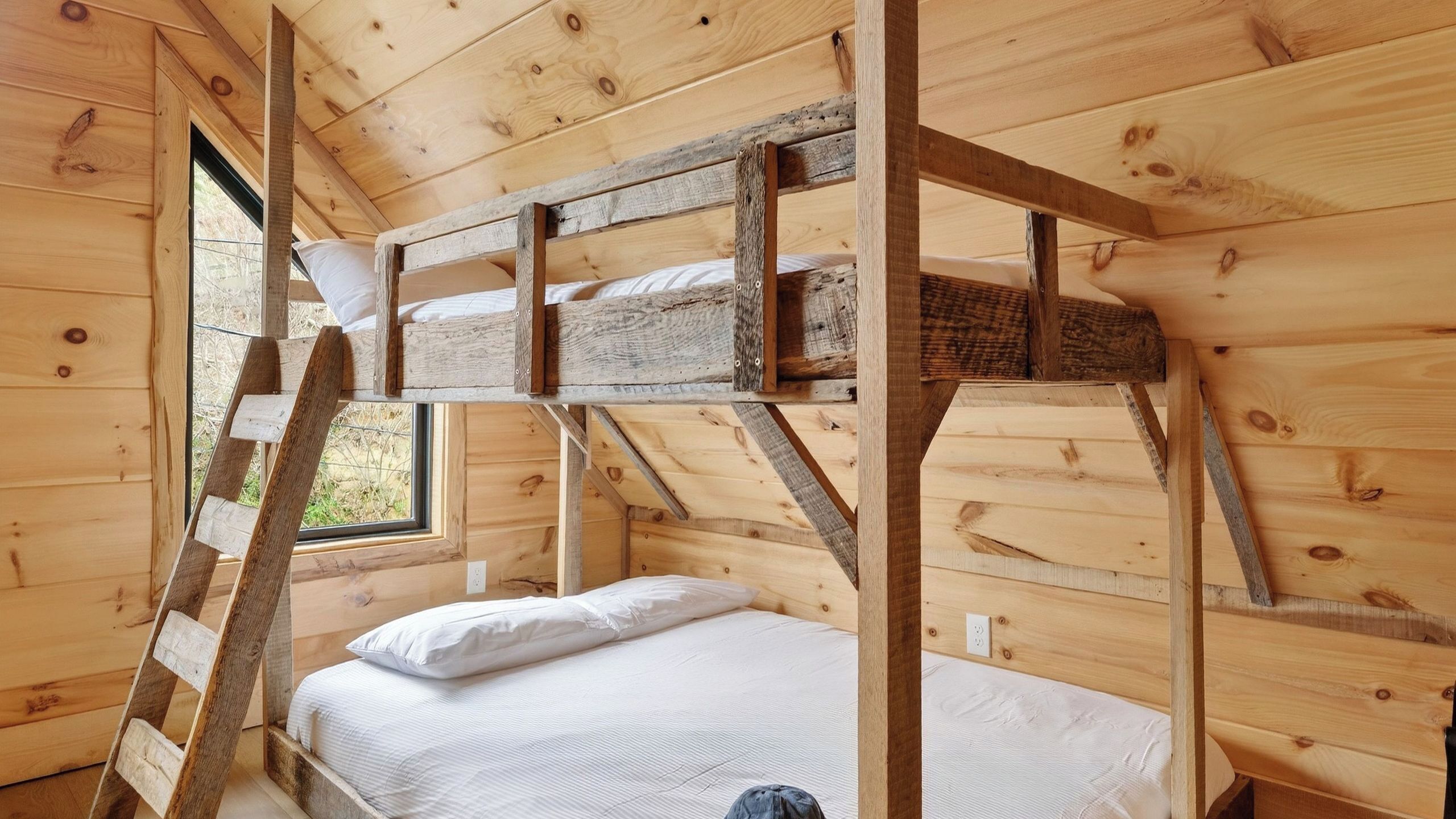 Una cabaña de madera con literas y una cama individual, con una ventana que ofrece vistas de la vegetación.
