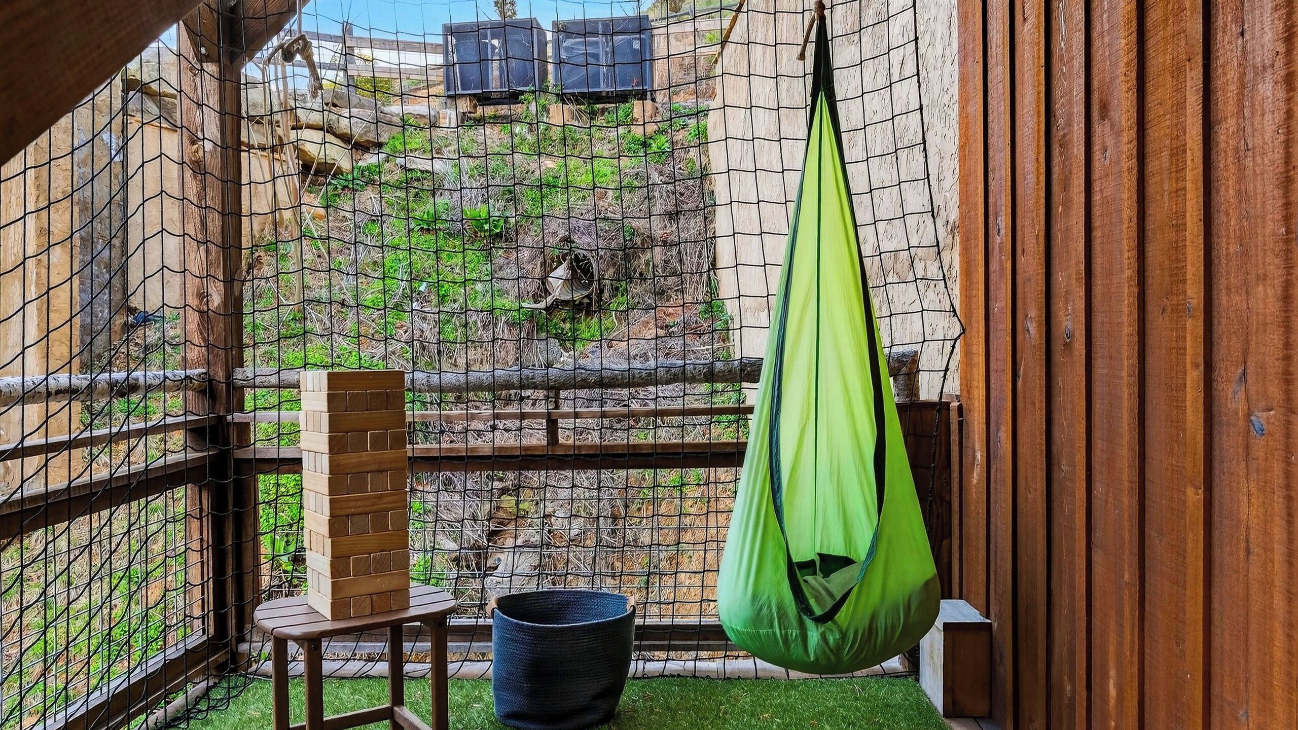 A balcony with a hanging chair, a small table, and a brick planter.