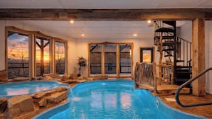 An indoor swimming pool with natural stone accents, wooden beams, and large windows with a sunset view. - Aspen Lodge by Avantstay Indoor Pool + Hot Tub + Sauna + Game Room + Mountain Views (Gatlinburg)