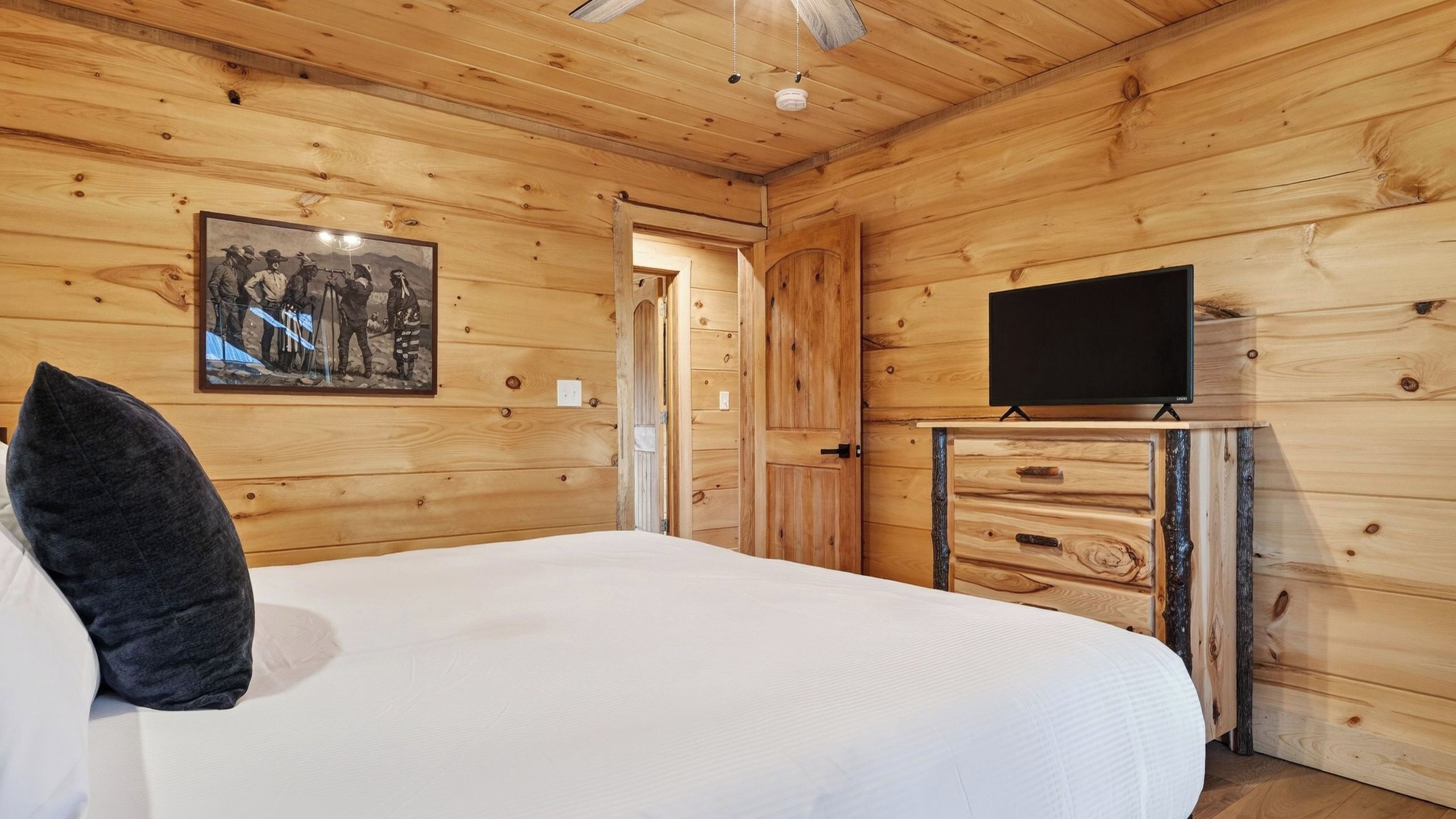 A wooden room with a bed, a dresser, a television, and a framed picture on the wall.