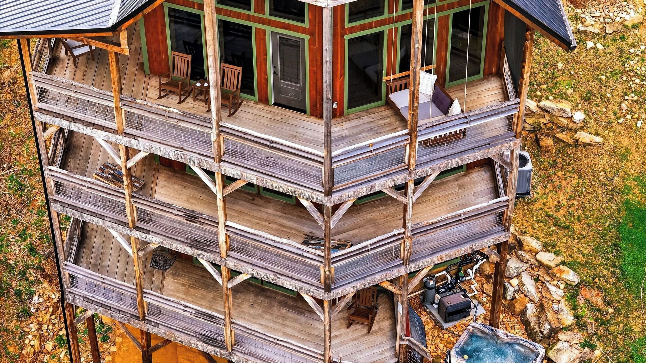 A multi-level wooden cabin with a balcony, outdoor seating, and a hot tub.