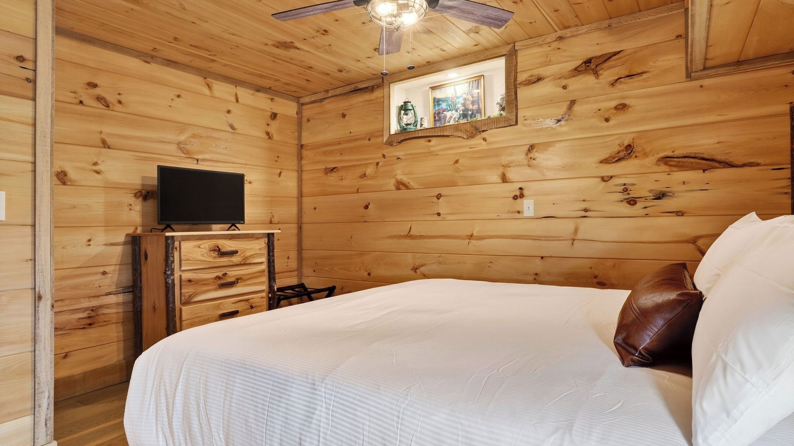 A wooden room with a bed, a dresser, a television, and a small window with a view.