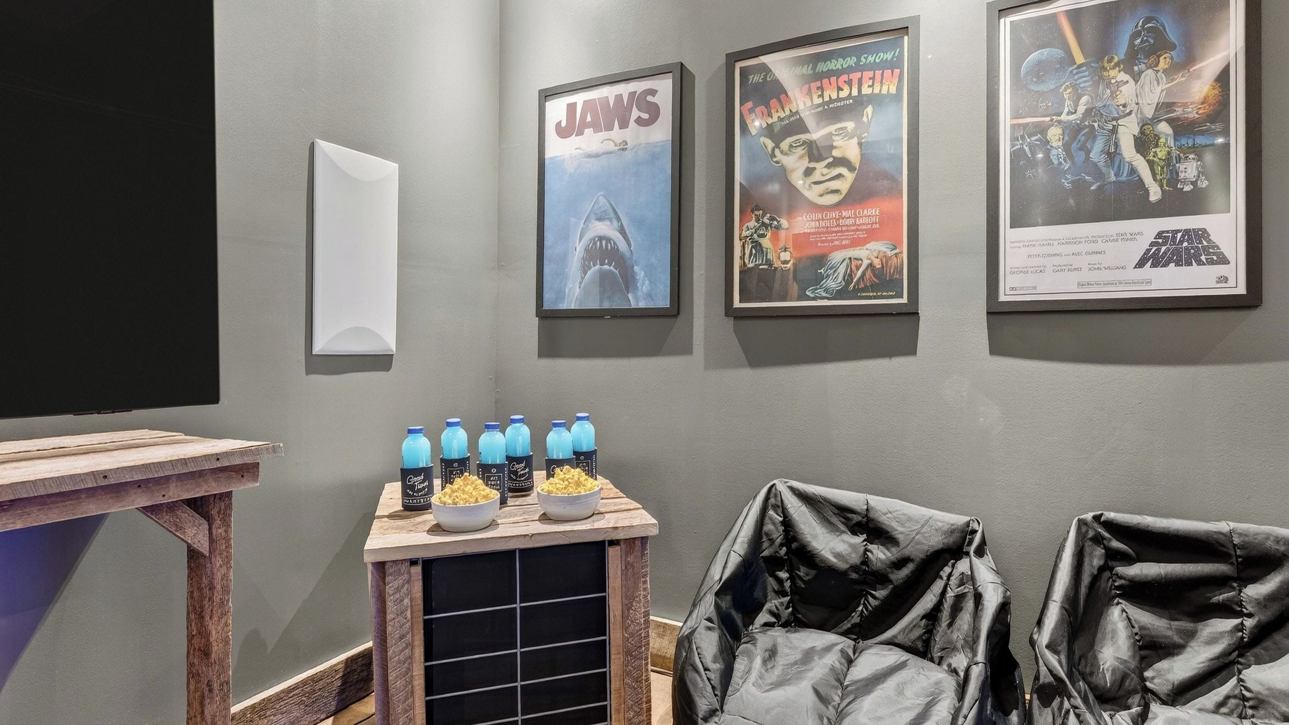 Ein Raum mit Projektionsleinwand, Postern von 'Jaws' und 'Frankenstein', einem Popcornstand und zwei schwarzen Ledersesseln.