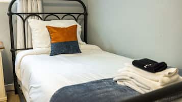 Ein Einzelbett mit Metallgestell, weißer Bettwäsche und einem blau-orangen Kissen.