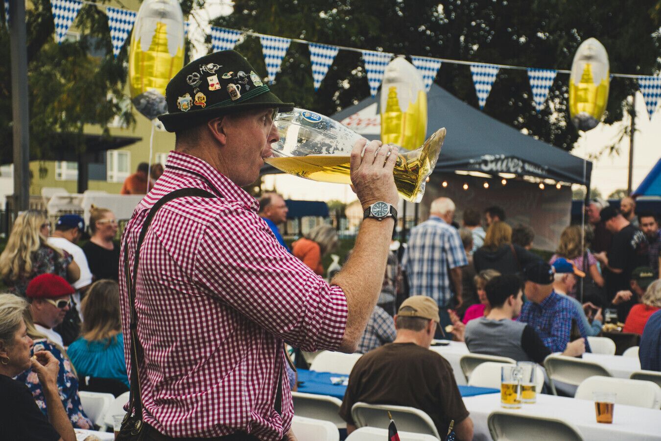 A person wearing a checkered shirt and a hat with badges, holding a large beer mug.