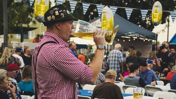 A person wearing a checkered shirt and a hat with badges, holding a large beer mug.