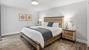 Une chambre à coucher avec un lit en bois, deux tables de chevet avec des lampes, un luminaire au plafond et deux œuvres d’art accrochées au mur.