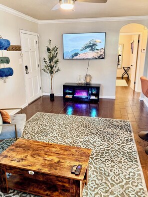 A living room with a flat-screen TV, a wooden coffee table, a patterned rug, and a potted plant. - Walk to OCU •Lazy Leopard Lounge •Stylish OKC Stay• 2 bedroom• KING & QUEEN (Oklahoma City)