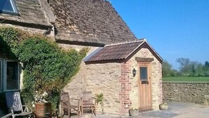 A stone building with a small attached structure, outdoor seating, and a stone wall. - Stable Cottage Battens Farm (Chippenham)