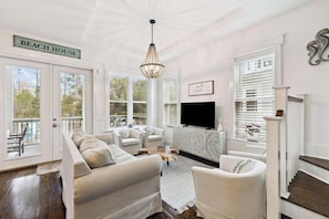 A living room with a sectional sofa, a fireplace, and a TV. There are large windows and a sign that reads 'BEACH HOUSE'. - Community Pool, Sleeps 10, Sunrise & Serenity, Bikes (Seagrove Beach)