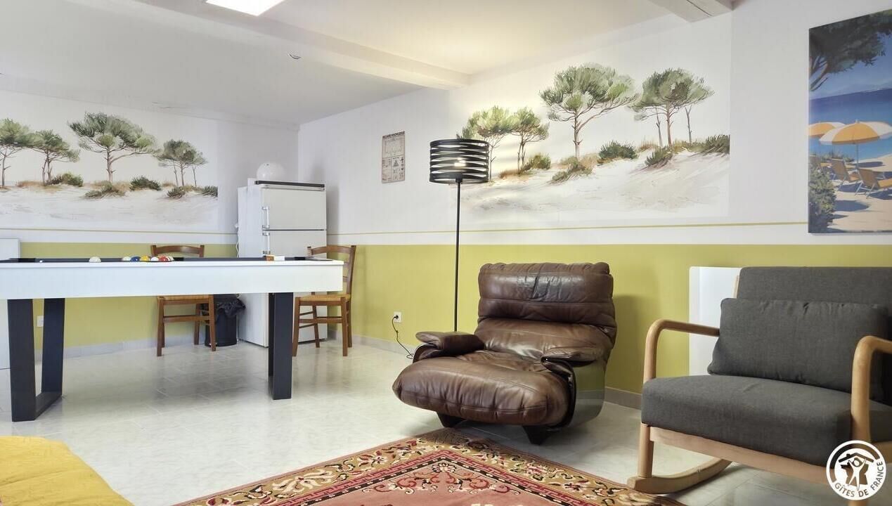 Een kamer met een pooltafel, een bruine lederen fauteuil, een grijze bank en kunstwerken aan de muren.