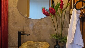 A bathroom with a stone sink, a mirror, a towel rack, and a decorative plant. - Ceiba EcoContainer / La Fortuna / Jacuzzi - AC - WIFI. (Agua Azul)