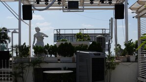 Una terraza en la azotea con una pérgola, una estatua, plantas en macetas y una silla de metal.