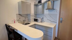 Una cocina moderna con encimera blanca, microondas integrado y fregadero de acero inoxidable.